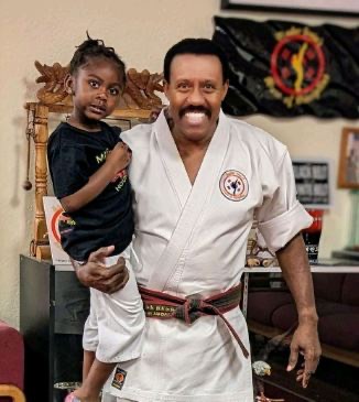 Master Irvin holding a young student in the school, both smiling.