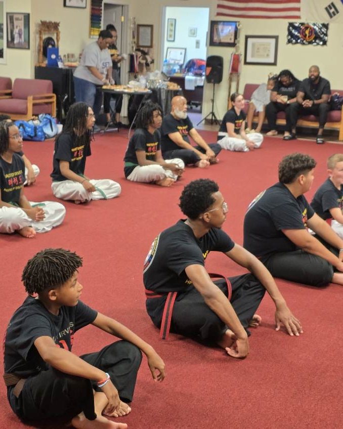 Students seated on the school floor listening to instruction.